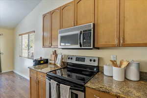 Kitchen featuring dark hardwood / wood-style flooring, stainless steel appliances, vaulted ceiling, and stone countertops