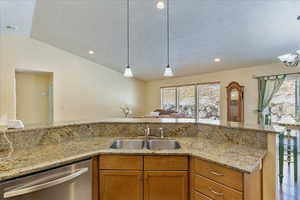 Kitchen featuring dishwasher, sink, vaulted ceiling, a textured ceiling, and light stone counters