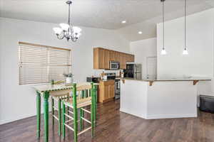 Kitchen featuring dark wood-style flooring, baseboards, a chandelier, brown cabinetry, and appliances with stainless steel finishes