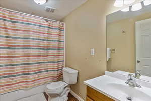 Full bathroom featuring a textured ceiling, vanity, shower / bath combo, and toilet