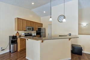 Kitchen with a kitchen breakfast bar, dark hardwood / wood-style flooring, stainless steel appliances, and decorative light fixtures