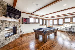 Game room with hardwood / wood-style floors, a stone fireplace, beamed ceiling, and billiards