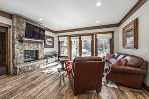 Living room with hardwood / wood-style flooring, a stone fireplace, and ornamental molding