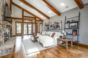 Living room featuring light hardwood / wood-style floors, a stone fireplace, beam ceiling, and french doors