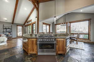 Kitchen with dark stone counters, decorative light fixtures, appliances with stainless steel finishes, a notable chandelier, and beam ceiling