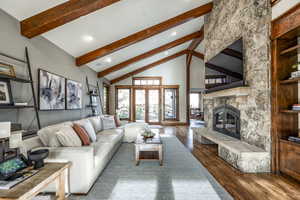 Living room featuring high vaulted ceiling, french doors, hardwood / wood-style flooring, a fireplace, and beam ceiling