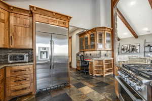 Kitchen featuring high quality appliances, decorative backsplash, built in desk, beamed ceiling, and stone countertops