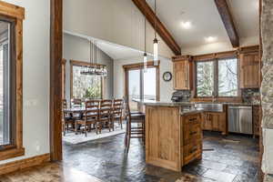 Kitchen featuring sink, stainless steel dishwasher, pendant lighting, decorative backsplash, and a breakfast bar