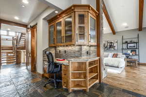 Bar with backsplash, light stone counters, beamed ceiling, and built in desk