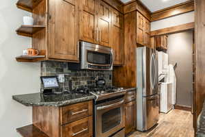 Kitchen featuring dark stone countertops, backsplash, appliances with stainless steel finishes, and light hardwood / wood-style flooring