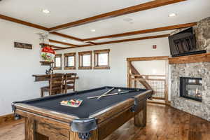 Rec room featuring beamed ceiling, a stone fireplace, wood-type flooring, and billiards