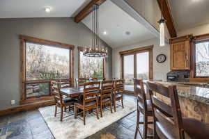 Dining space featuring vaulted ceiling with beams, plenty of natural light, and an inviting chandelier