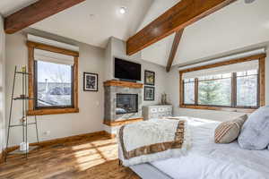 Bedroom with hardwood / wood-style floors, vaulted ceiling with beams, a fireplace, and multiple windows