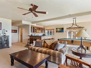 Living room with ceiling fan, light colored carpet, bar, and pool table