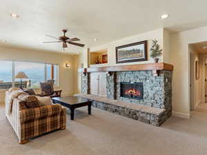 Living room featuring ceiling fan, a stone fireplace, and light colored carpet