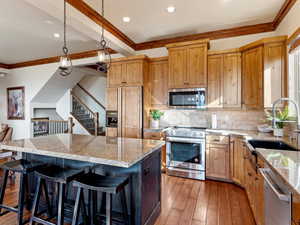 Kitchen with hardwood / wood-style floors, a center island, sink, ornamental molding, and appliances with stainless steel finishes