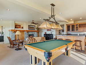 Playroom with bar area, light colored carpet, a stone fireplace, and billiards