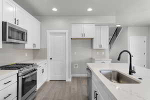 Kitchen featuring appliances with stainless steel finishes, sink, light stone counters, and white cabinets