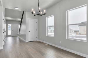 Unfurnished dining area with light hardwood / wood-style floors and a notable chandelier