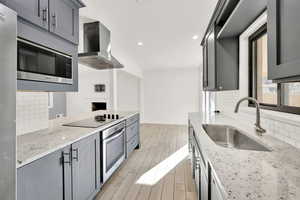 Kitchen featuring decorative backsplash, wall chimney exhaust hood, light hardwood / wood-style flooring, sink, and appliances with stainless steel finishes