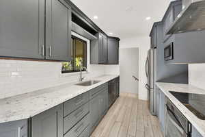 Kitchen with stainless steel appliances, light hardwood / wood-style floors, sink, light stone counters, and wall chimney range hood