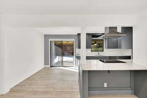 Kitchen with light hardwood / wood-style floors, sink, kitchen peninsula, wall chimney exhaust hood, and decorative backsplash