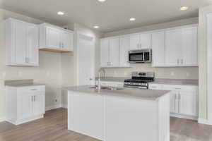 Kitchen with white cabinetry, sink, stainless steel appliances, a center island with sink, and light wood-type flooring