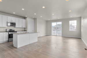 Kitchen featuring light wood-type flooring, stainless steel appliances, a kitchen island with sink, sink, and white cabinetry