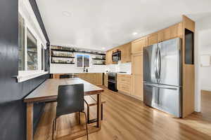 Kitchen with sink, light hardwood / wood-style flooring, light brown cabinetry, appliances with stainless steel finishes, and a breakfast bar area