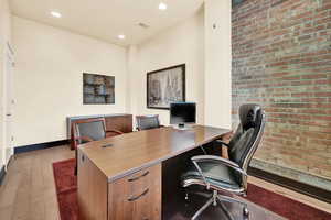 Office area with light hardwood / wood-style floors and brick wall