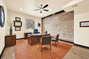 Office space featuring light hardwood / wood-style flooring, ceiling fan, and brick wall