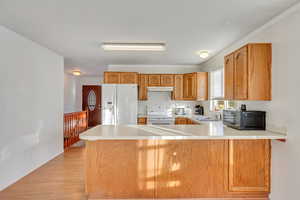 Kitchen featuring kitchen peninsula, sink, light hardwood / wood-style floors, and white appliances