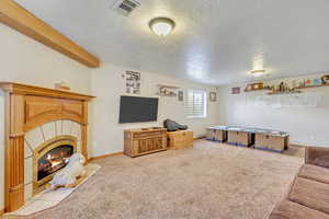 Carpeted living room with a fireplace, beam ceiling, and a textured ceiling