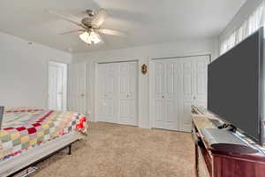 Bedroom with ceiling fan, light colored carpet, and two closets