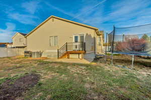 Rear view of house with a yard, central AC unit, and a trampoline