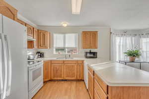 Kitchen featuring light wood-type flooring, white appliances, kitchen peninsula, and sink