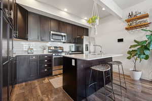 Kitchen featuring subway tile backslash, an island with sink, a breakfast bar area, and appliances with stainless steel finishes