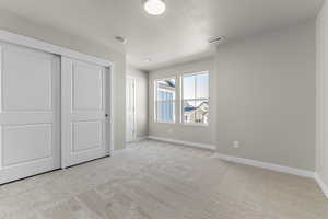 Unfurnished bedroom featuring light carpet, a closet, and a textured ceiling