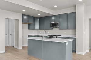 Kitchen featuring a kitchen island with sink, sink, light wood-type flooring, and appliances with stainless steel finishes