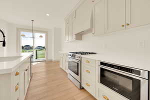 Kitchen featuring hanging light fixtures, stainless steel appliances, light hardwood / wood-style flooring, white cabinets, and custom range hood