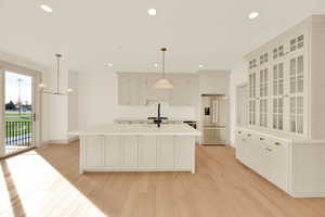 Kitchen featuring light hardwood / wood-style flooring, stainless steel fridge with ice dispenser, hanging light fixtures, and an island with sink