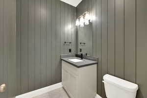 Bathroom featuring vanity, toilet, and wooden walls