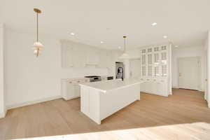 Kitchen featuring white cabinetry, stainless steel appliances, an island with sink, pendant lighting, and light hardwood / wood-style floors