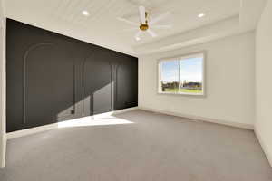 Empty room with a tray ceiling, ceiling fan, wood ceiling, and light carpet