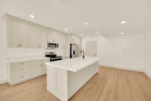 Kitchen featuring light wood-type flooring, stainless steel appliances, white cabinetry, and a center island with sink