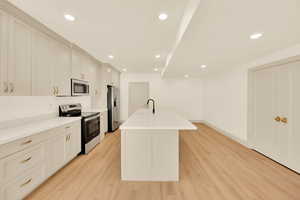 Kitchen with sink, an island with sink, stainless steel appliances, and light hardwood / wood-style floors