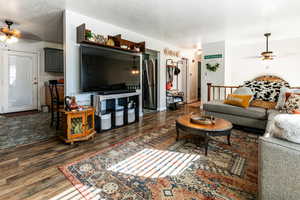 Living room with a textured ceiling, ceiling fan, and dark wood-type flooring