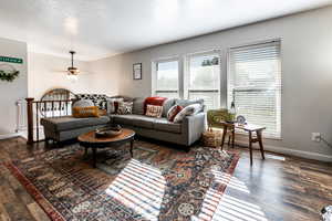 Living room featuring a textured ceiling, ceiling fan, and dark wood-type flooring