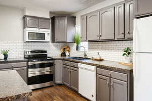 Kitchen featuring white appliances, dark hardwood / wood-style floors, gray cabinetry, and backsplash