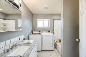 Laundry area with washing machine and clothes dryer, light tile patterned floors, a textured ceiling, and sink